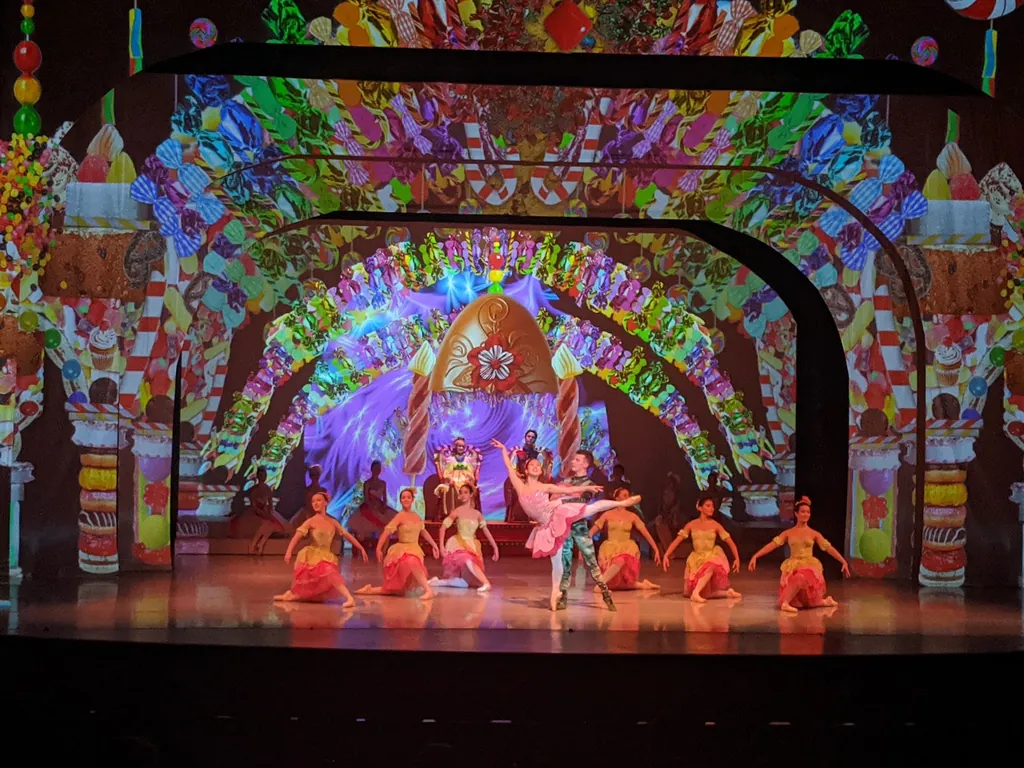 Spectacle de danse coloré, danseurs en costumes et grand décor projeté — concepteur d’éclairage, compagnie Ballet Ouest de Montréal.